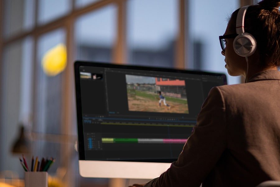 female employee wearing headphones and looking at computer screen working on sports video editing, highlight video special